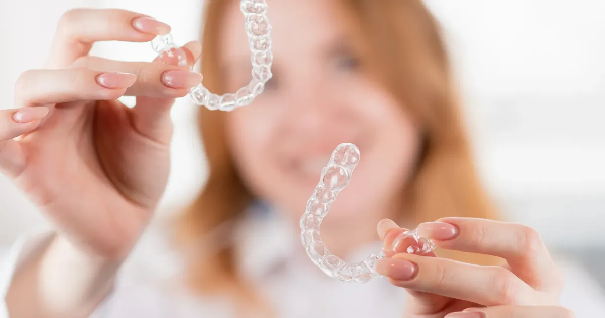 Mujer sosteniendo alineadores invisibles transparentes.