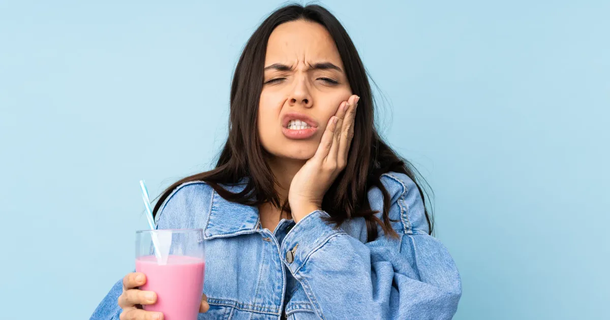 Una mujer toma algo frio que le produce sensibilidad dental